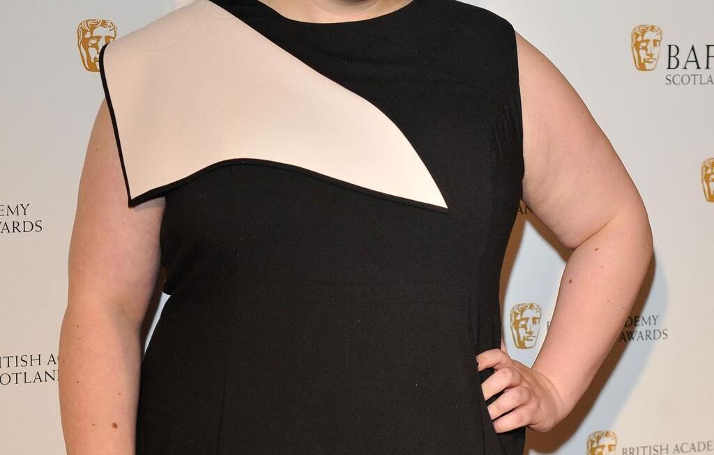 Scottish actress Sharon Rooney posing in a promotional photo for the BBC reality show Celebrity Traitors series two, Scottish actress Sharon Rooney known for My Mad Fat Diary and Barbie looking toward the camera, Official cast announcement graphic for Celebrity Traitors featuring actress Sharon Rooney, Sharon Rooney standing in front of a dark castle backdrop for The Traitors promotional material