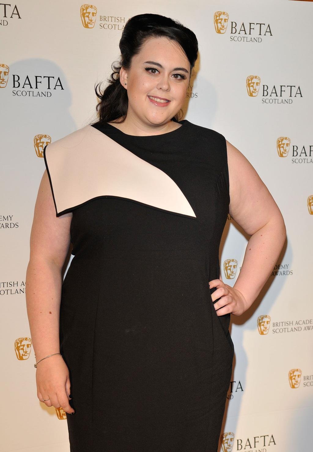 Scottish actress Sharon Rooney posing in a promotional photo for the BBC reality show Celebrity Traitors series two, Scottish actress Sharon Rooney known for My Mad Fat Diary and Barbie looking toward the camera, Official cast announcement graphic for Celebrity Traitors featuring actress Sharon Rooney, Sharon Rooney standing in front of a dark castle backdrop for The Traitors promotional material